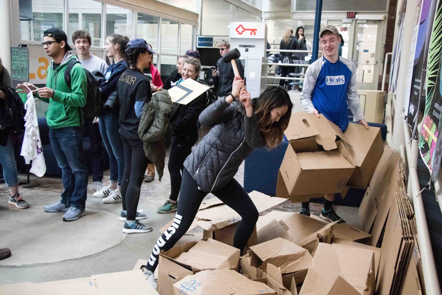 (Left to right) An attendee of the RecycleMania Carnival makes a bag out of an old t-shirt, while another smahes carboard boxes with a rubber hammer.