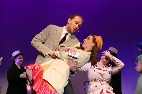 Billy Flynn (Milo Cassarino) holds Mary Sunshine (Mariah Hamburg) as both of them sing and reach for their guns in a comedic performance.