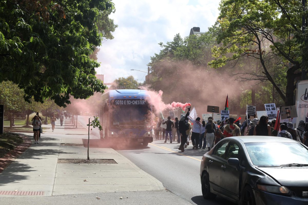 The protesters pass an RTA bus on Adelbert Road as they purposefully avoid being on campus property. One protester holds a smoke flare that fills the air.